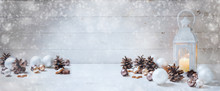 Wide Christmas Background With A Candle Light Lantern, Baubles, Cinnamon Stars And Cones On Rustic White Wood, Panorama Format For Website Banner, Copy Space