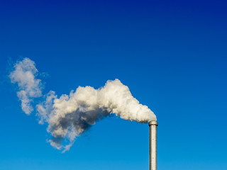 A metallic chimney giving off a heavy cloud of white smoke against a deep blue sky.