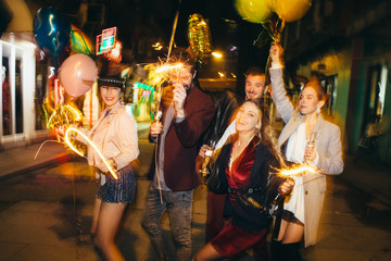 Group of happy friends going on the party, having fun at the street and drinking champagne. New year party. Birthday party 