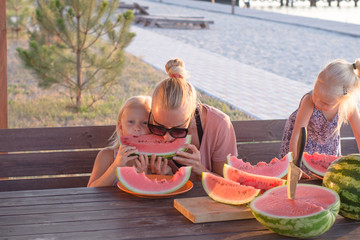 Mother with two kids eat watermelon slices outdoors in summertime  