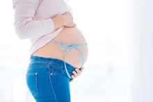 Baby Boy. Pregnant Woman Supporting Her Round  Tummy That Tied With Blue Ribbon  While Standing In Profile