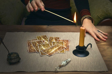 Tarot cards on fortune teller desk table. Future reading. Woman lights a candle by matches.