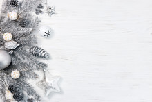 Silver Christmas Tree Branches Decorated With Toys, Cones And Garland Lights On White Wooden Desk. Holiday Background.
