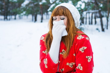 woman was ill with the flu. epidemic of virus diseases. Influenza winter. Young Woman in Winter Clothing Blowing Nose with tissue paper outdoor. Caucasian female in snow park sneezing.
