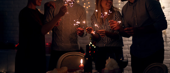 Group of smiling friend having fun with sparkles at home for Christmas in the night.