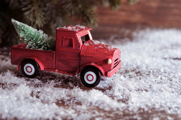 Red car carrying a Christmas fir tree on the snow background. Concept for Xmas times and Winter holidays. Copy space.