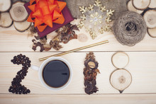 2018 Inscription Of Coffee Beans, Cup, Dry Flowers And Wooden Slices, A Dark Purple Gift Box With An Orange Bow, A Golden Snowflake And A Straw, A Skein Of Threads, Light Wooden Background, Top View