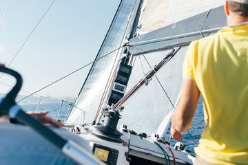 Professional sailor or yachtsowner controls sailboat with mainsail and spinnaker up, by observing data and information from devices on mast, wind speed and power