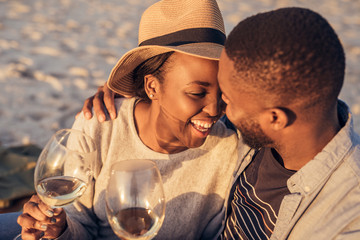 Romantic young African couple drinking wine together at the beach