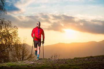 Wall Mural - Man athlete with trail beard trail with sticks at sunset