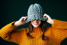 Beautiful Young Happy Smiling Girl Hiding Her Eyes Under Trendy Grey Big Loop Knitted Beanie Hat. Model Wearing Winter Sweater. Close Up
