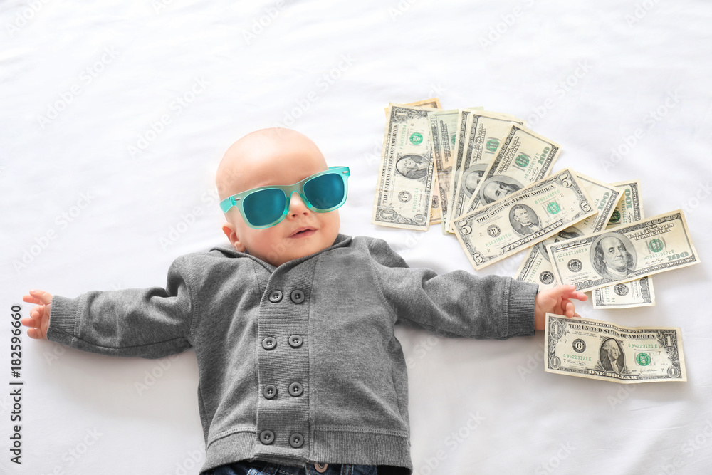 Cute boy with money on white bedsheet