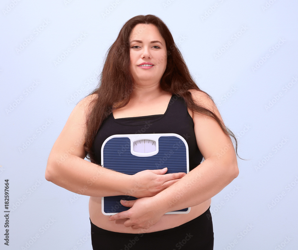 Overweight woman holding scales on light background