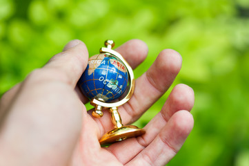 The front view of Man hand is holding small globe outdoor. Concept of travelling and adventure, blur background