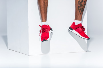 low section of african american man in red sneakers sitting on grey