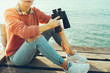© tinyakov - Young Girl Sits On A Pier With Binoculars In Hand And Enjoys The View Of Nature