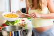 Pregnant woman cooking pasta in domestic kitchen putting it into hot water