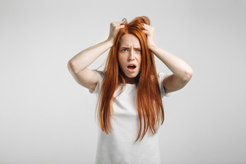 Closeup portrait of emotional redhead girl on white background with strong expression of fear, round eyes, open mouth and hands pressed to top of head, showing astonishment and shock