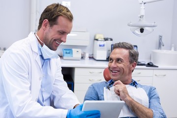 Dentist discussing over digital tablet with male patient