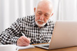 © Prostock-studio - Mature man using laptop and writing in notepad