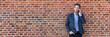 © Maridav - Business man talking on mobile phone panoramic banner of brick wall background texture. Happy young businessman using cellphone in urban setting wearing smart casual suit.