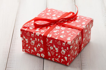 Wall Mural - Christmas gift or present box with a red holiday print tied with ribbon on white wooden background