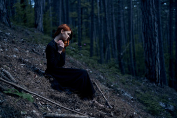 beautiful woman sitting in a black dress in a dark forest