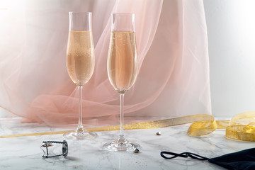 Two flute glasses with champagne on marble background. Pink transparent fabric. Soft light. Horizontal composition