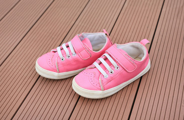 Pair of pink baby leather sneakers on wood plank background.