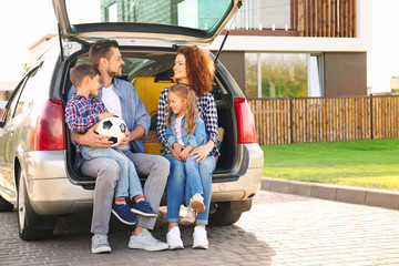 Young family with children sitting in car trunk near house