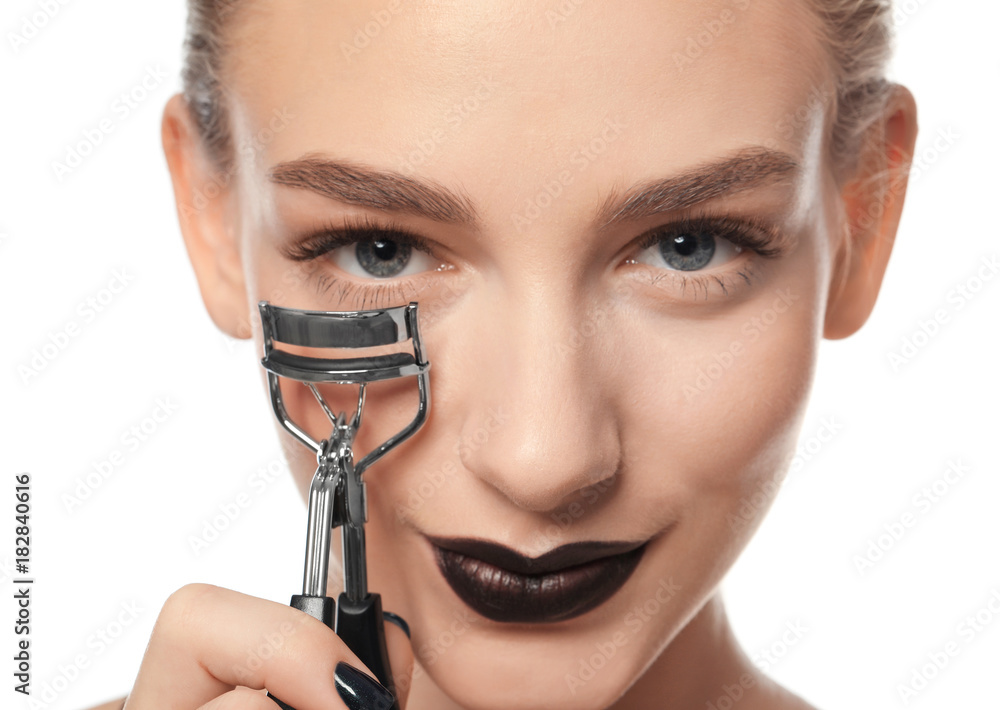 Beautiful young woman with eyelash curler on white background, closeup