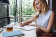 © LUMINA IMAGES - Pretty blonde Caucasian woman writing in her notebook at home office.
