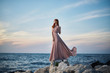 © SHOTPRIME STUDIO - Beautiful young woman in a long dress standing by the sea, rocks
