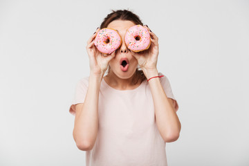 Wall Mural - Portrait of an excited pretty girl holding donuts at her face