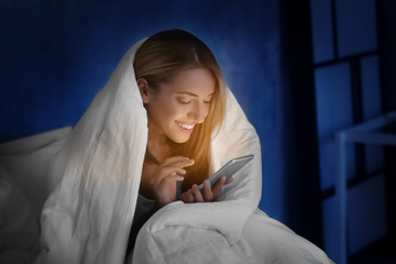 Poster - Beautiful young woman with mobile phone in bed at night