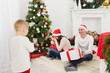 © ViDi Studio - Happy young cheerful parents with cute little son in red hat. Child boy in light room at home with decorated New Year tree and gift boxes. Christmas good mood. Family, love and holiday 2018 concept.