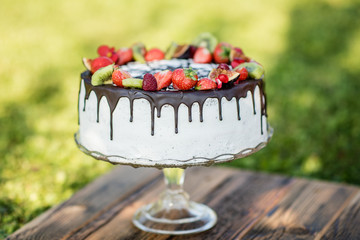 close up of a birthday wedding cake with white cream drizzled with chocolate and decorated with fruit berries