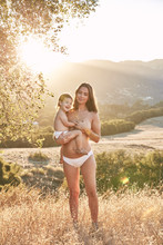 Portrait of pregnant woman and her baby standing outdoors during summer
