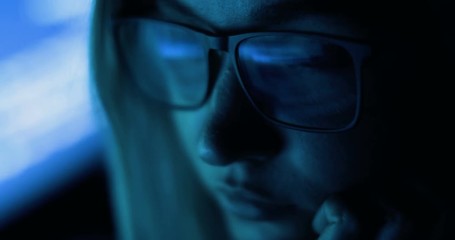 woman working with computer, hacking and writing. Computer screen and code reflected in woman's glasses.