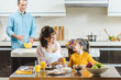 © LIGHTFIELD STUDIOS - cheerful family, mother with daughter sitting at table and looking at each other with father on background