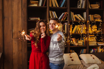 christmas or valentine concept happy young couple holding sparklers hugging and smiling while celebrating new year