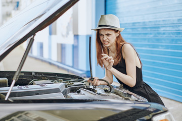 Young beautiful woman in a white hat repairing a car on a city street