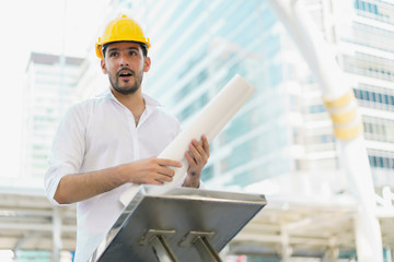 Engineer man wearing safety helmet and hold blueprint document at construction site. concept of work office, security consult, job control, development and business process.