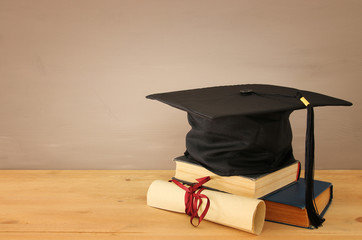 Image of graduation black hat over old books next to graduation on wooden desk. Education and back to school concept.