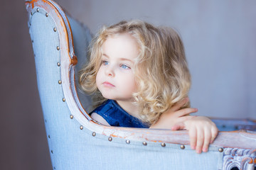 Beautiful pretty toddler girl sitting in arm-chair, looking away. Beautiful eyes.