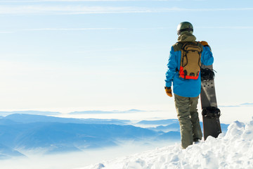 Young snowboarder standing next to snowboard thrusted into snow and looking at a beautiful scenery before him