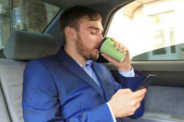 Wall Mural - Young businessman drinking coffee on back seat of taxi car