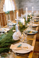 winter, warmness, comfort concept. in the dining hall there is new year feast table decorated with lots of burning high candles and fresh green conifer branches