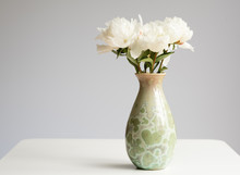 Closeup Of White Peonies In Green Vase On Table Against Grey Background With Copy Space