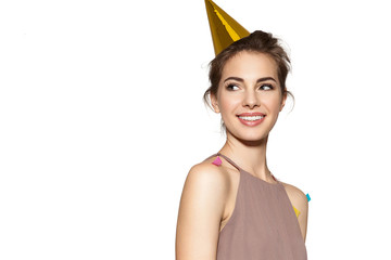 Happy smiling girl with festive hat on head and colored confetti on dress. Isolated on white background. Close up portrait of adorable laughing birthday girl.